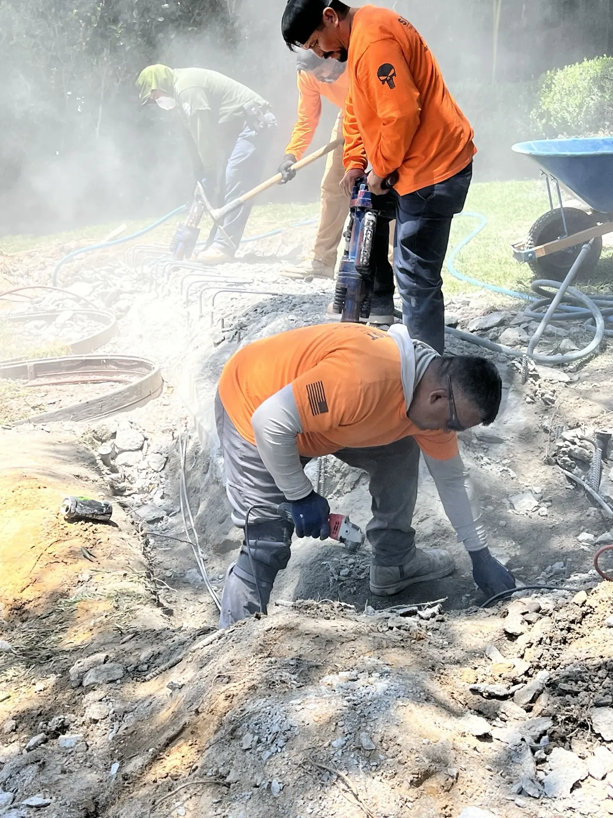 Crew breaking out concrete by hand with jackhammers as dust rises