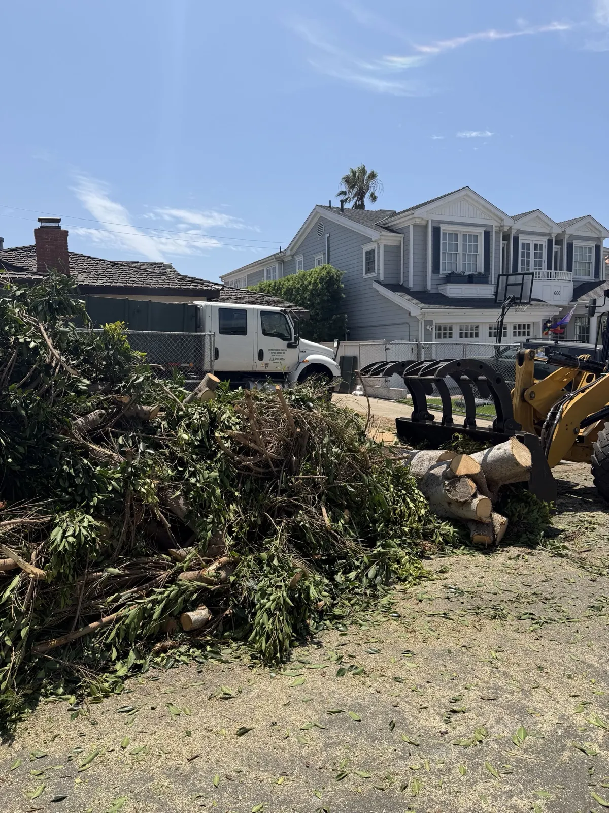 Pile of cut brush and branches beside a grapple loader on a cleared residential lot