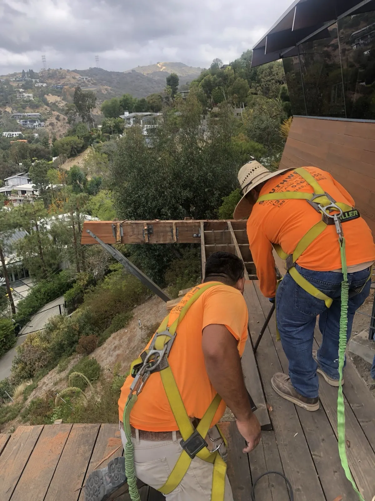 Two crew members in safety harnesses taking apart a hillside deck above Los Angeles