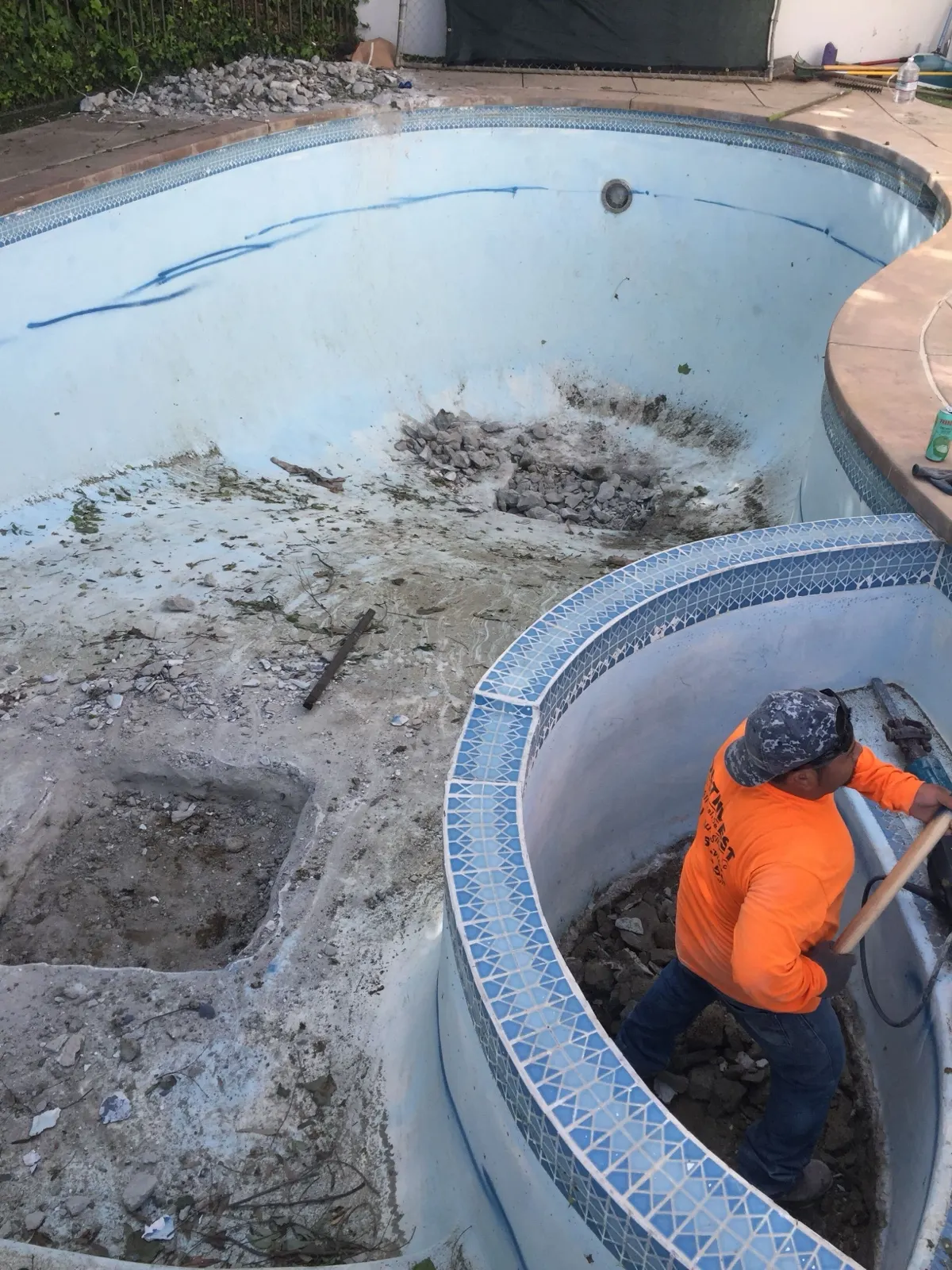 A crew member breaking up the shell of a drained swimming pool with a jackhammer