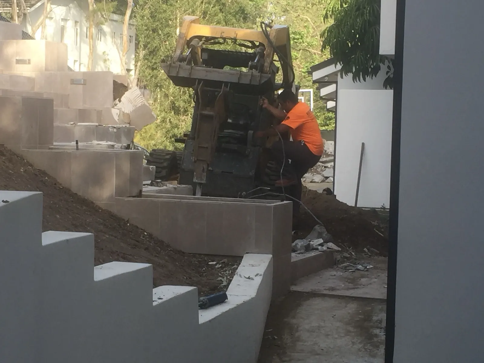 Skid steer working down a run of terraced concrete retaining walls on a slope